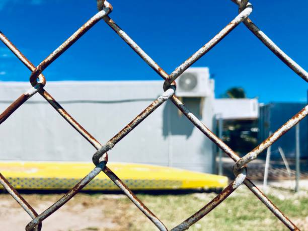 istock Fence with rusty white painted old cage and white blurred building with blue sky on the back 1139787421