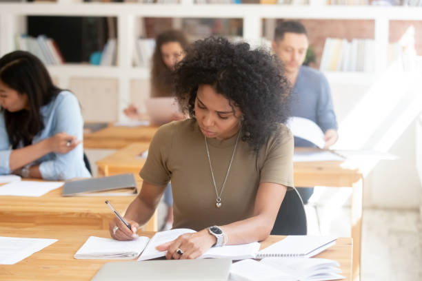 Focused african female college high school student studying in classroom Focused serious african american female college high school student studying in multi ethnic classroom group writing essay in exercises book passing final exam test working on university assignment multi ethnic group college student group of people global communications stock pictures, royalty-free photos & images