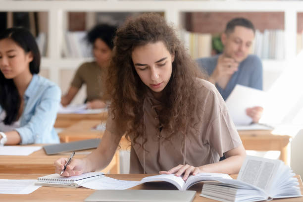 istock Teen girl studying with textbook writing essay learning in classroom 1139791101