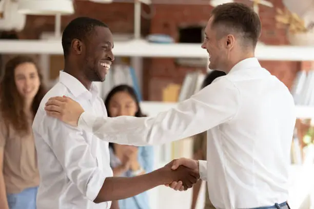 Photo of Caucasian executive handshaking promoting successful happy african worker expressing gratitude