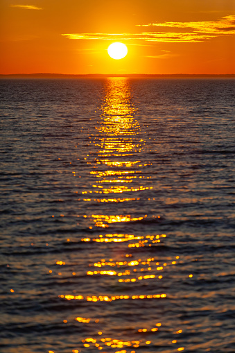 bright orange sun with reflection in the water during sunset over the sea