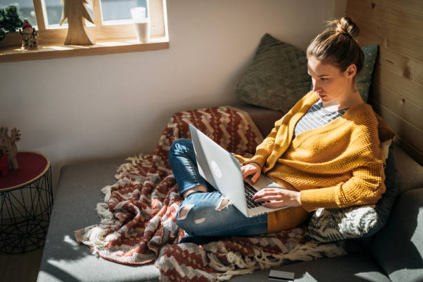 молодая женщина, используя ноутбук в уютном солнечном доме - credit card women laptop electronic banking стоковые фото и изображения