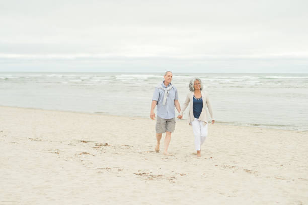 istock Senior couple holds hands as they walk on the beach 1139793023