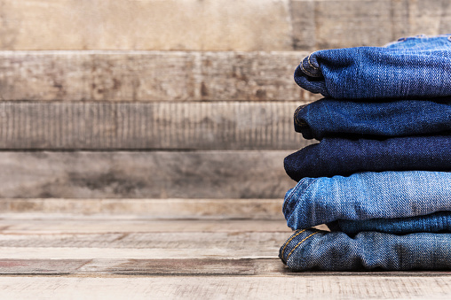 Stack of folded blue jeans on old wood background  with copy space