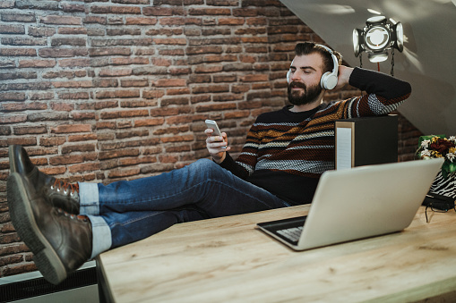Relaxed man using headphones and mobile phone in the office