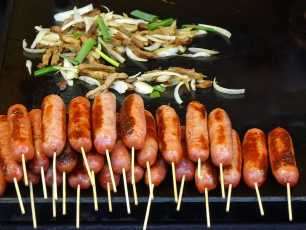 An outdoor vendor roasts fresh sausages and fries pork and leaks