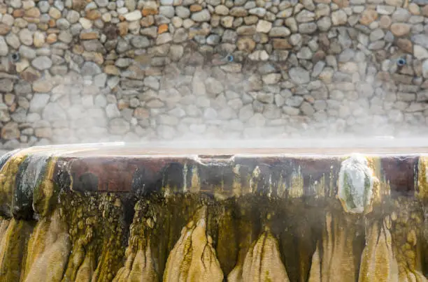 Hot vapor lingering over a hot spring well with stone wall in the background.
