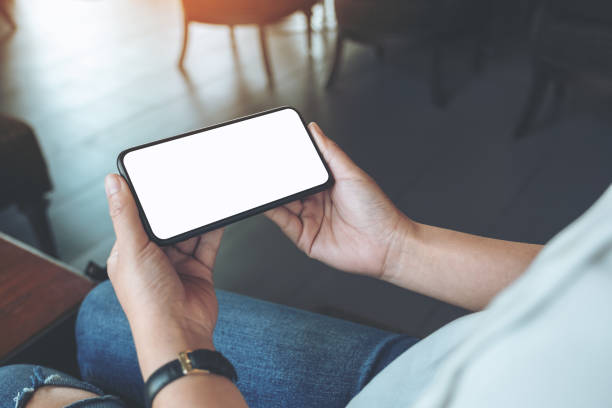istock Mockup image of woman's hands holding black mobile phone with blank white screen horizontally in cafe 1139821349