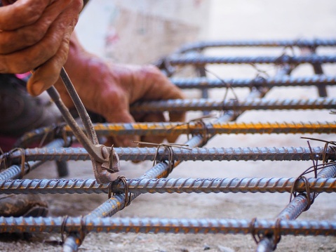 close up builder worker hands use pincers and wires for knitting metal rods to secure rebar before concrete is poured over it. building construction and industry concept