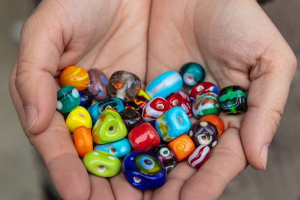 palma de la mano mostrando excepcionales perlas de vidrio hechas a mano originales en varios colores variados. - glass bead fotografías e imágenes de stock