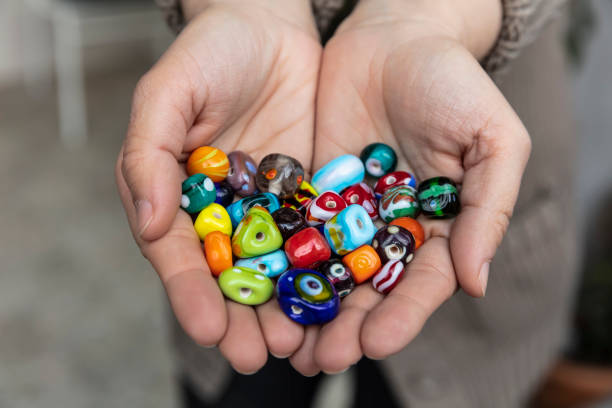 palma de la mano mostrando excepcionales perlas de vidrio hechas a mano originales en varios colores variados. - bead glass making jewelry fotografías e imágenes de stock