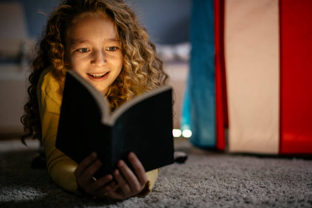 linda chica leyendo un libro en casa - child bedtime imagination dark fotografías e imágenes de stock