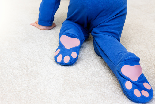 Rear view of a child crawling in a onesie with non-slip safety patches on the feet.