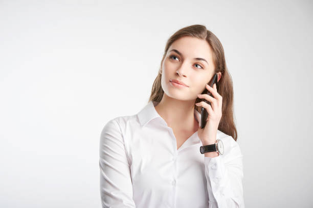 Portrait of smiling young businesswoman using her mobile phone and talking with somebody while standing against at isolated white background.