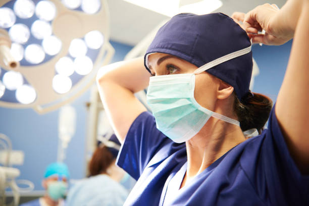 side view of young female surgeon tying her surgical mask - surgeon imagens e fotografias de stock