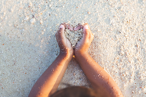 Child girl holding sand make heart shape in hands and playing on the beach in summer vacation