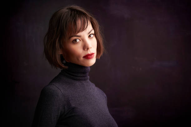 istock Beautiful young woman standing at dark background and looking at camera 1139850004