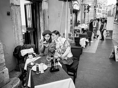 Rome, Italy, Nov 15 - Some men observe two tourists sitting pleasantly outside a restaurant in a street in the historic center of Rome, absorbed in their conversation.