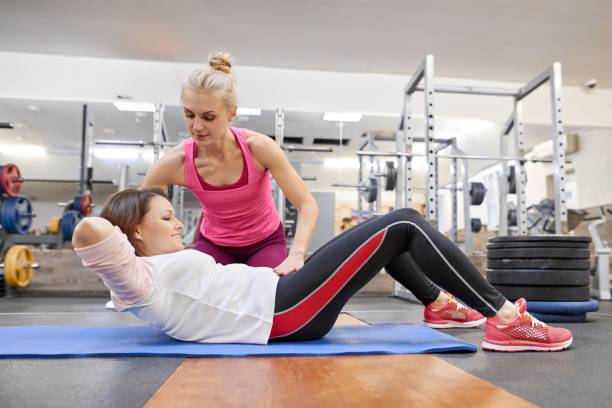 middle-aged woman doing sports exercise in fitness center. personal gym trainer assisting mature woman. health fitness sport age concept - secrecy instructor exercising individuality imagens e fotografias de stock