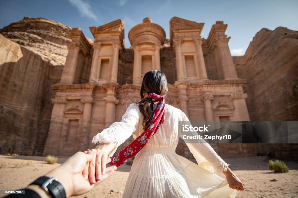 Asian woman tourist in white dress holding her couple hand at Ad Deir or El Deir, the monument carved out of rock in the ancient city of Petra, Jordan. Travel UNESCO World Heritage Site in Middle East Travel Stock Photo
