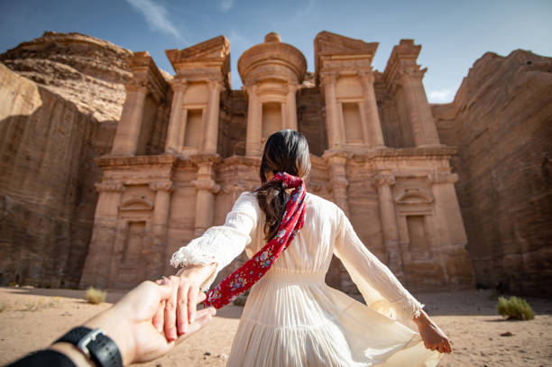 Asian woman tourist in white dress holding her couple hand at Ad Deir or El Deir, the monument carved out of rock in the ancient city of Petra, Jordan. Travel UNESCO World Heritage Site in Middle East stock photo