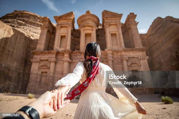 Asian Woman Tourist In White Dress Holding Her Couple Hand At Ad Deir Or El Deir The Monument Carved Out Of Rock In The Ancient City Of Petra Jordan Travel Unesco World Heritage Site In Middle East Stock Photo - Download Image Now