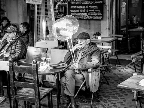 Rome, Italy, Dec 26 - A cute elderly gentleman with his grandson's balloons, enjoying a relaxing moment sitting outside a café in Piazza Campo dei Fiori, in the historic center of Rome.