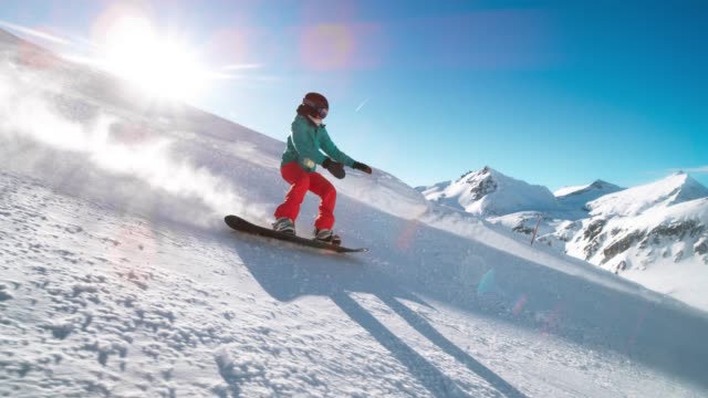 SLO MO TS Female snowboarder riding down the sunny mountain slope covered in fresh powder