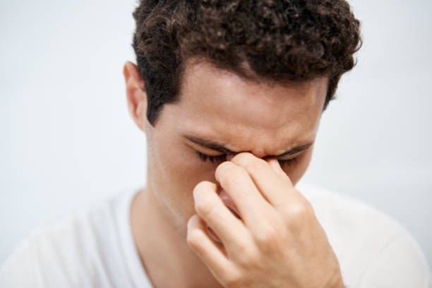 Young man frowns, holding head and nose A young man looks down, unhappy or in pain, holding the top of his nose and concealing his face. holding nose stock pictures, royalty-free photos & images
