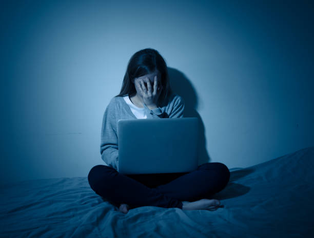 Scared and intimidated teenager crying being bullied on laptop suffering cyberbullying and harassment. Child victim of bullying stalker social media, online challenges and dangers of internet. stock photo