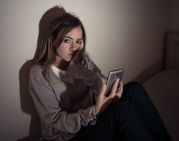 Young teenager girl suffering mobile cell phone addiction feeling lonely and depressed having insomnia needing to be connected sitting on bed late at night. In internet and mobile addiction concept. stock photo