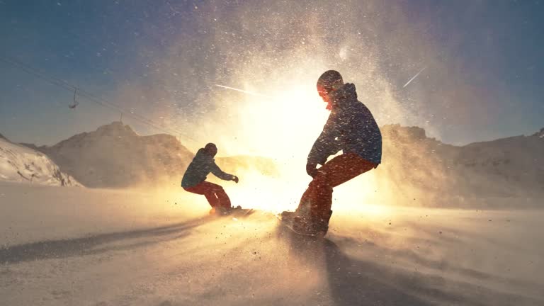 SLO MO TS Two snowboarders riding down a slope towards the sun