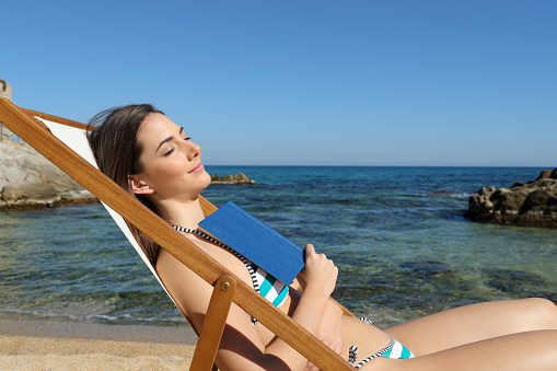 Tourist sleeping on the beach holding a book