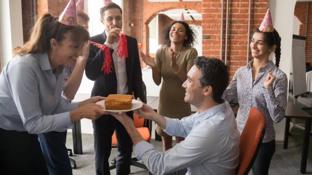 istock Friendly diverse employees in party hats presenting cake congratulating colleague 1139873840