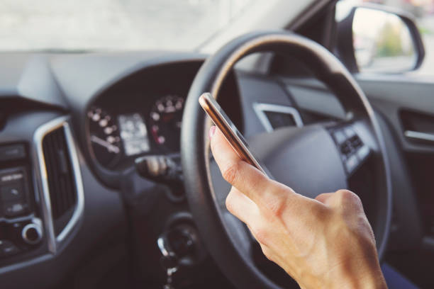 Close up of female hand holding smatrphone and typing while driving. Woman texting message using cellphone sitting in car. Answering call while being at wheel. Hand with phone on car cabin background cierre de mano femenina sosteniendo smatrphone y escribiendo mientras se conduce. mujer enviando mensajes de texto usando teléfono celular sentado en el coche. contestar llamada mientras está en el volante. mano con teléfono en el fondo de la cabina del