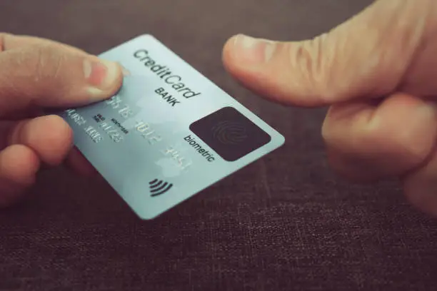 Close up of male hands holding credit card with fingerprint scanner and embedding the thumb to pay online. Concept of using biometric technology in banking. Cardholder touching his biometric card