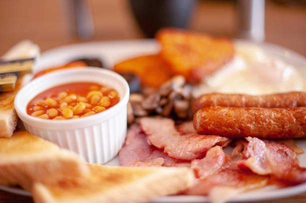 Full English Breakfast Close up with Shallow Focus Full English Breakfast Close up with Shallow Focus with Fried Eggs, Baked Beans, Bacon, Mushrooms, Hash Browns, Sausages, Tomato, Black Pudding, Toast and Butter Portions english breakfast stock pictures, royalty-free photos & images