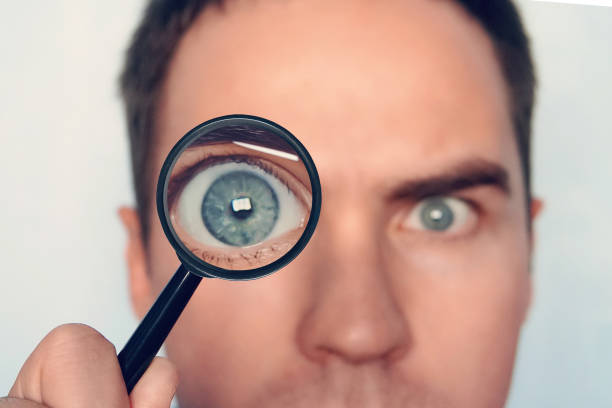 close up of man's face with the loupe close to one eye on white background. view to round human eye through the magnifiying glass. curious researcher. looking through magnifier intently. eye focus. - transparent holding glass focus on foreground imagens e fotografias de stock