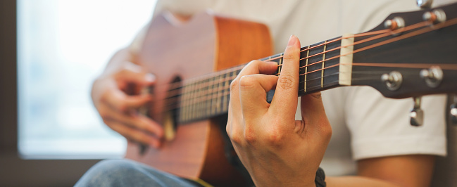 close up young hipster asian teenager boy playing classical guitar for practice musical skill at university dormitory , millennial lifestyle concept