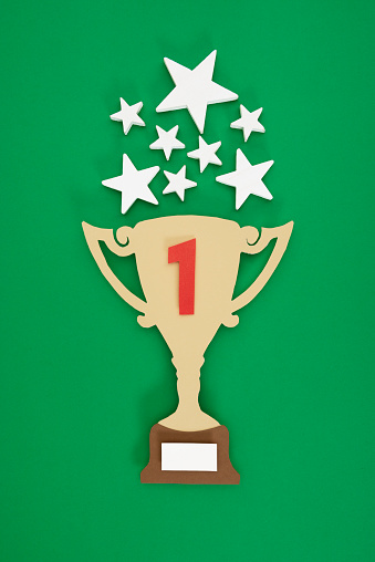 Yellow trophy made of paper with number 1 in red on it on green background with stars over it.