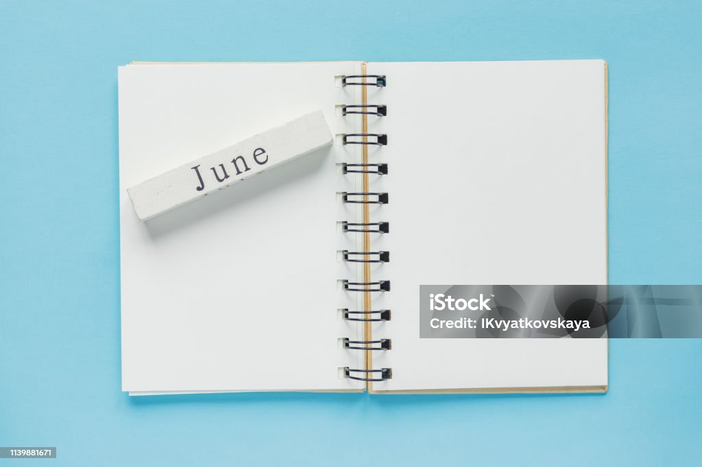 Clean spiral note book for notes and messages and june wooden calendar bar on blue background. Minimal business flat lay Blank Stock Photo