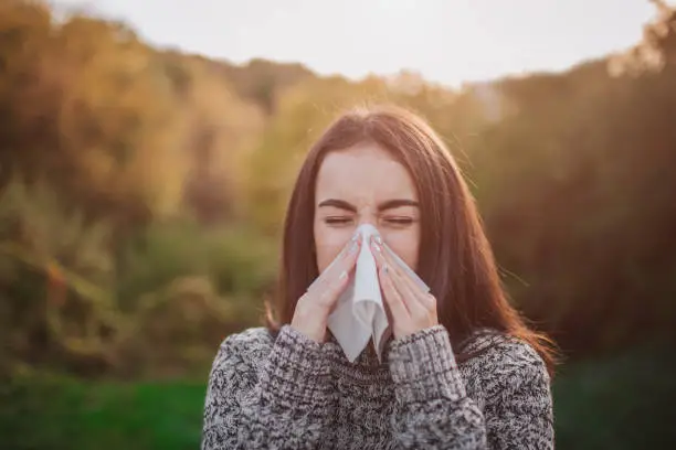 Photo of young woman with handkerchief. Sick girl has runny nose. Female model makes a cure for the common cold on an autumn background