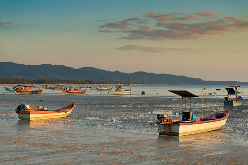 Pakarang beach (Takua Pa) at sunset. There are long tail boats aground or moored offshore lit by the setting sun.