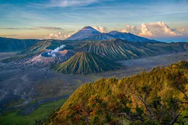 An early morning panoramic view of the volcano Gunung Bromo (with white smoke, altitude 2.329 meters) and Gunung Semeru (highest mountain in the background, 3.676 meters). Image was taken before sunrise, there are also some stars visible in the sky.