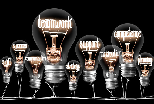 Photo of light bulbs group with shining fibers in a shape of Teamwork, Competence and Support concept related words isolated on black background