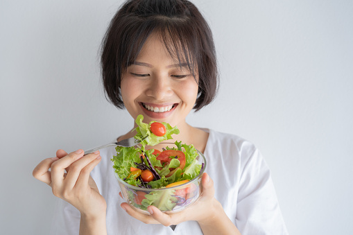 Portrait of asian woman smiling and eating salad on white background, healthy and lifestyle concept