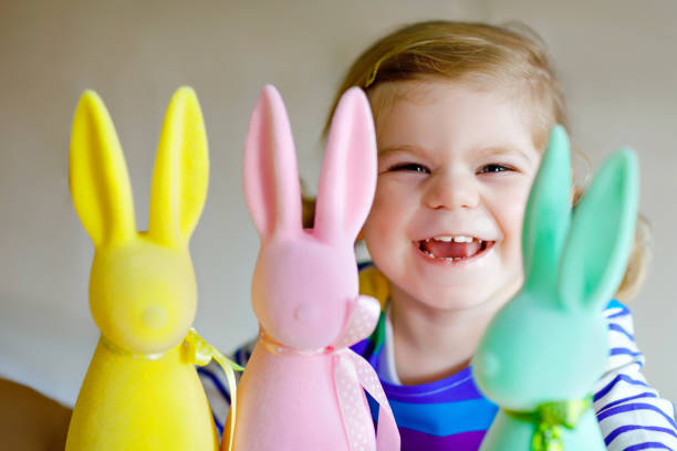 ピンク、黄色と緑のイースターデコレーションバニーとの楽しみを持っている3色のパステルバニー幸せな赤ちゃんの子供とかわいい小さな幼児の女の子。家族の休日を楽しむ愛らしい健康的 - easter easter bunny fun humor ストックフォトと画像