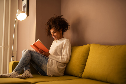 Portrait of a beautiful african american smiling woman reading a book at home.