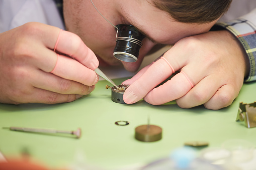 Close up of unrecognizable factory worker assembling intricate  mechanical watch, copy space