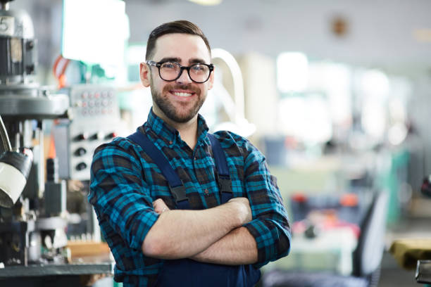 Cheerful Worker at Plant Waist up portrait of cheerful factory worker looking at camera while posing in workshop standing with arms crossed industrial building stock pictures, royalty-free photos & images